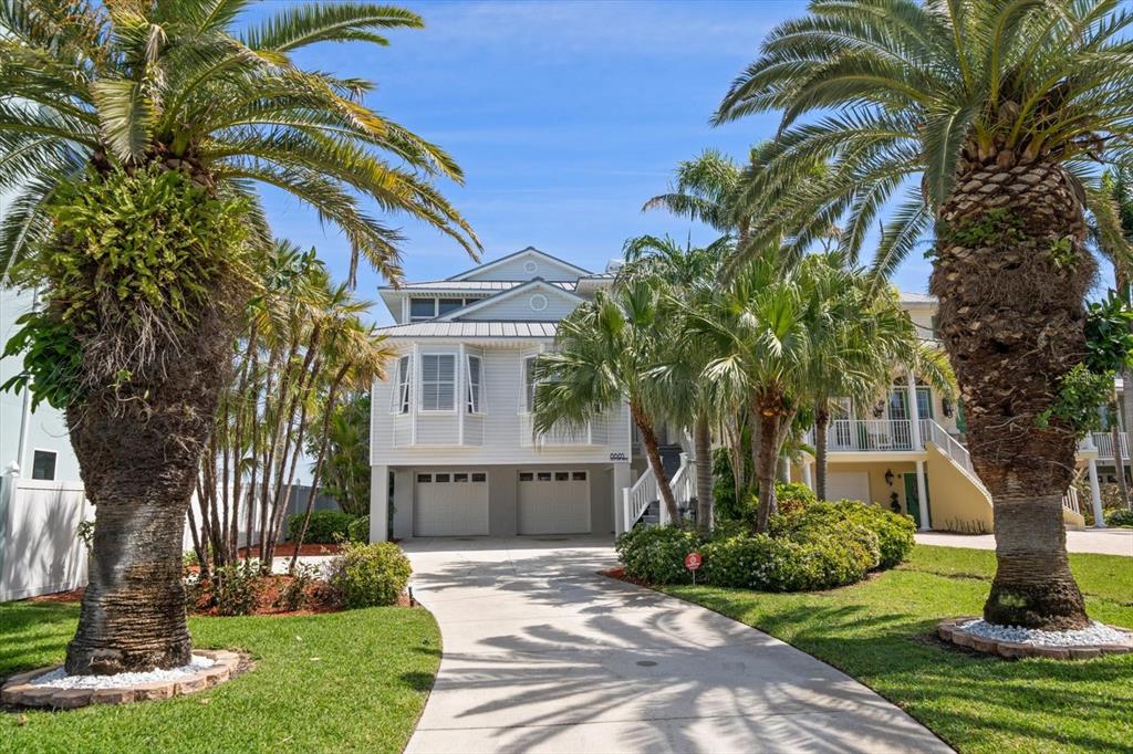 A two-story house with a white exterior, two garage doors, and palm trees in front — 8685 E BAY DRIVE, TREASURE ISLAND, FL
