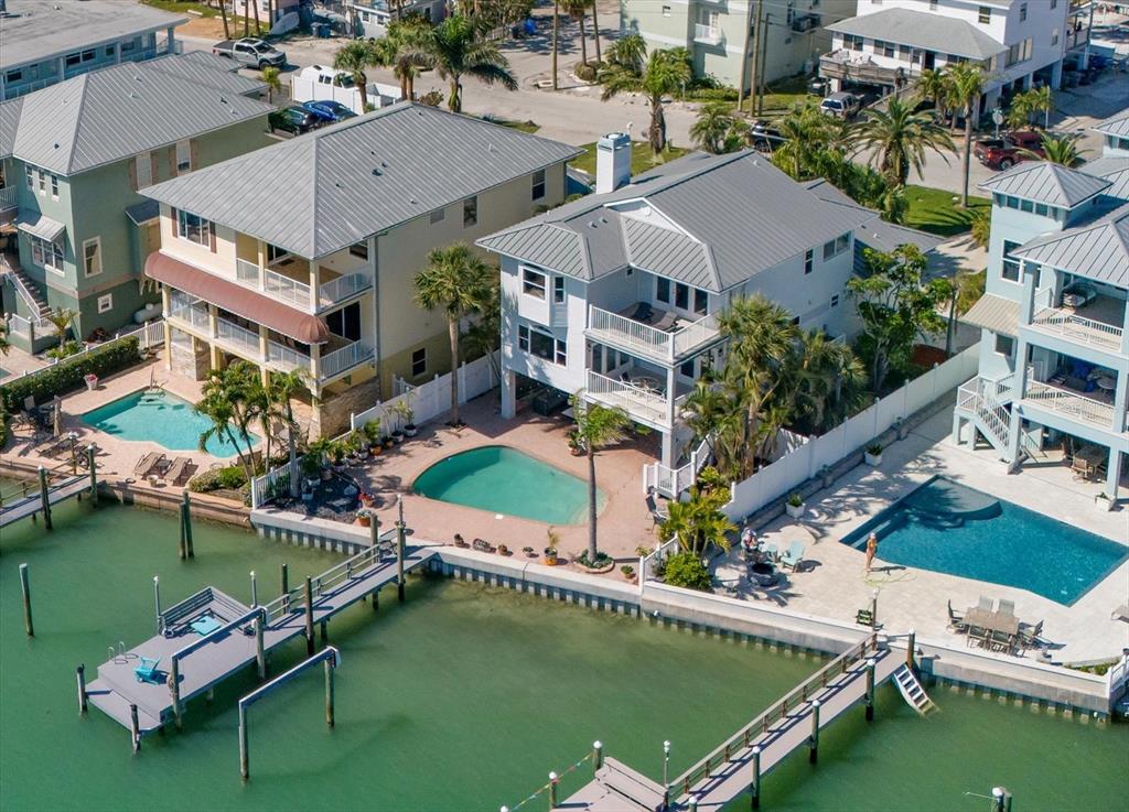 An aerial view shows three waterfront houses with private pools, docks, and metal roofs — 8685 E BAY DRIVE, TREASURE ISLAND, FL
