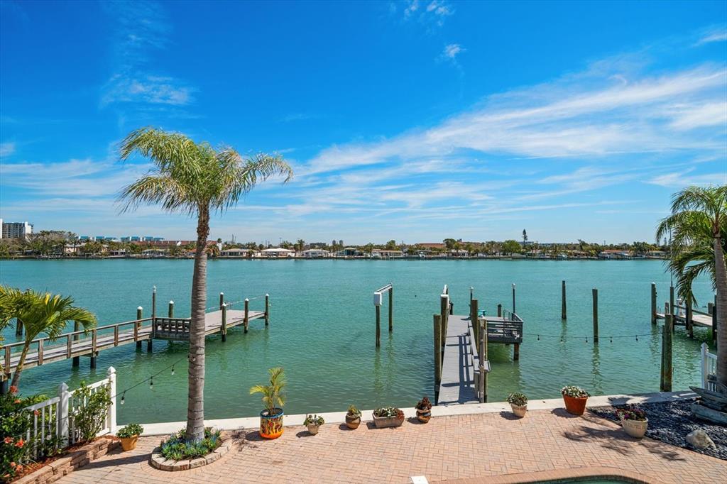 A brick patio overlooks a calm waterway with two wooden boat docks and palm trees — 8685 E BAY DRIVE, TREASURE ISLAND, FL