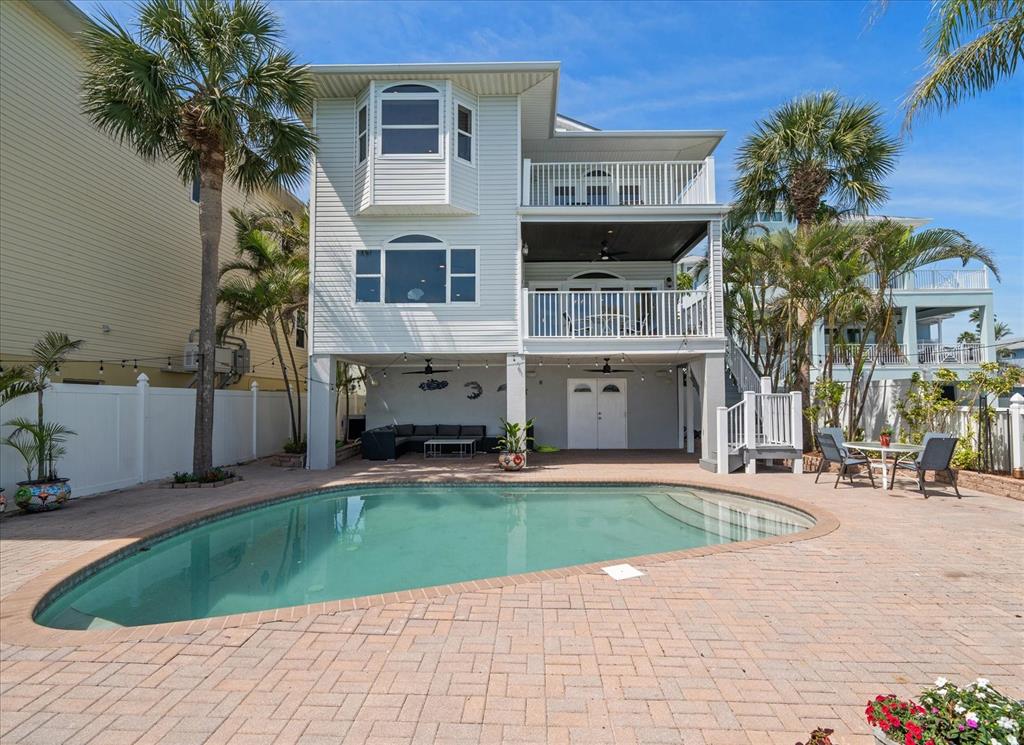 A three-story house with a pool and patio area sits in a fenced backyard — 8685 E BAY DRIVE, TREASURE ISLAND, FL