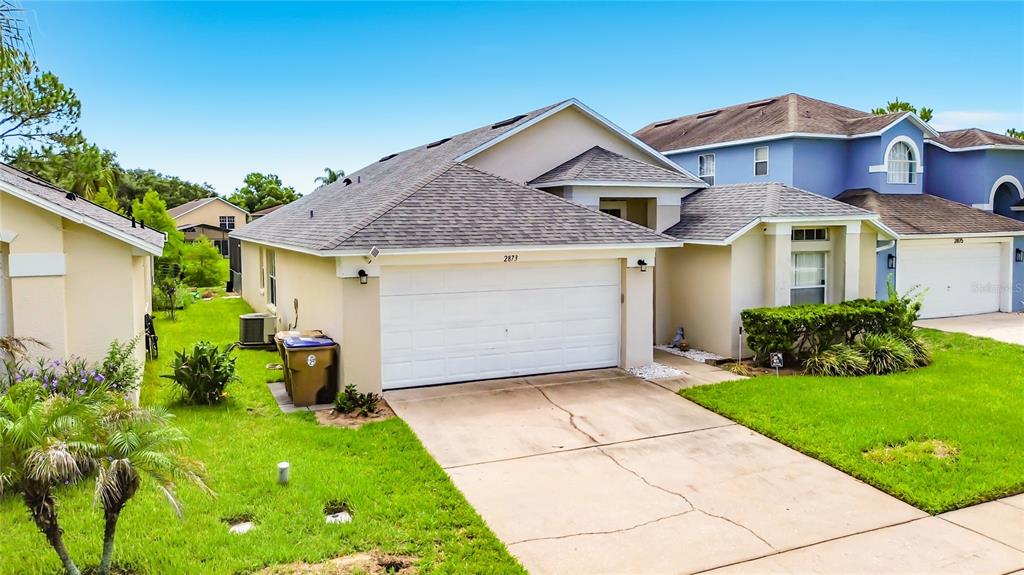 A suburban house with a white garage door, beige siding, and a concrete driveway — 2873 BLOOMING ALAMANDA LOOP, KISSIMMEE, FL