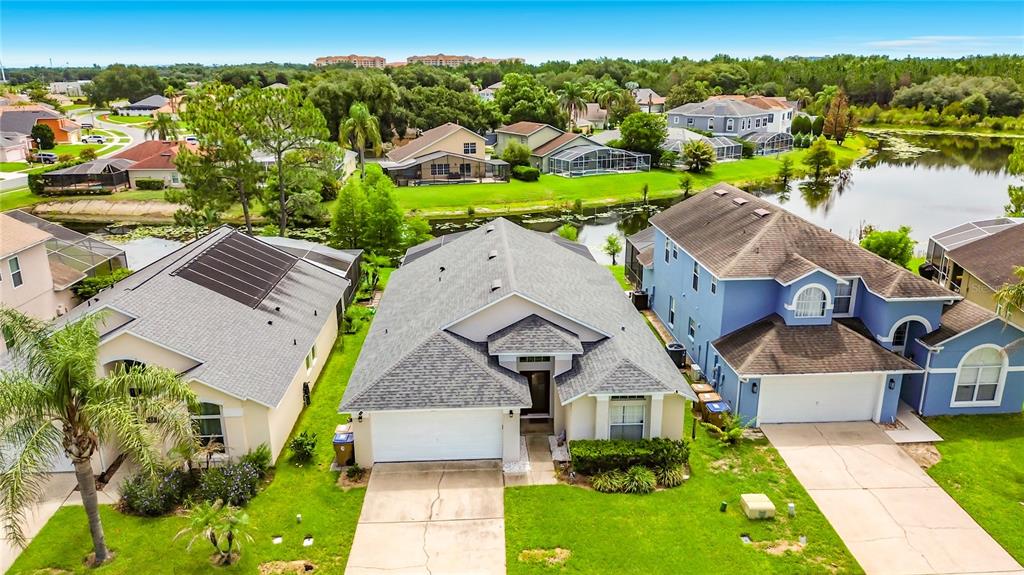 An aerial view shows three suburban houses with driveways and lawns near a small lake — 2873 BLOOMING ALAMANDA LOOP, KISSIMMEE, FL