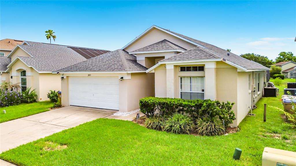 A single-story suburban house with a beige stucco exterior, a two-car garage, and green landscaping — 2873 BLOOMING ALAMANDA LOOP, KISSIMMEE, FL