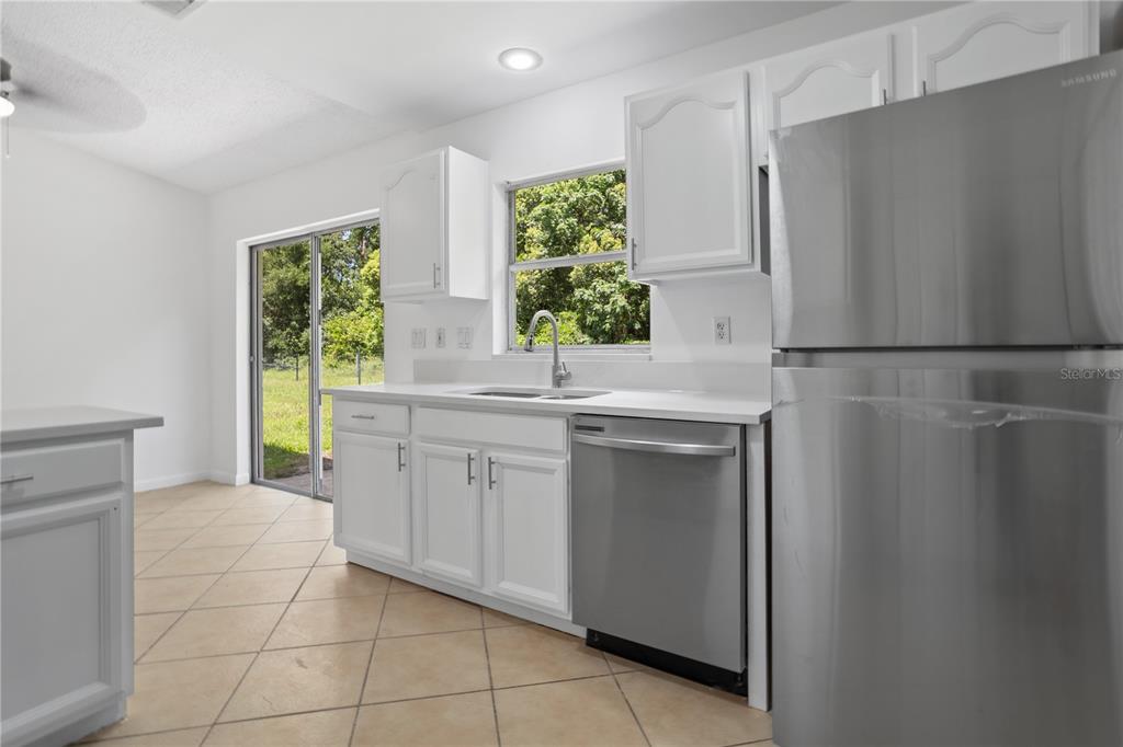 A bright kitchen features white cabinets, stainless steel appliances, and a sliding glass door — 1921 BONNEVILLE DRIVE, ORLANDO, FL