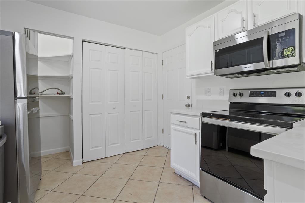 A kitchen features white cabinets, stainless steel appliances, tile flooring, and a walk-in pantry — 1921 BONNEVILLE DRIVE, ORLANDO, FL