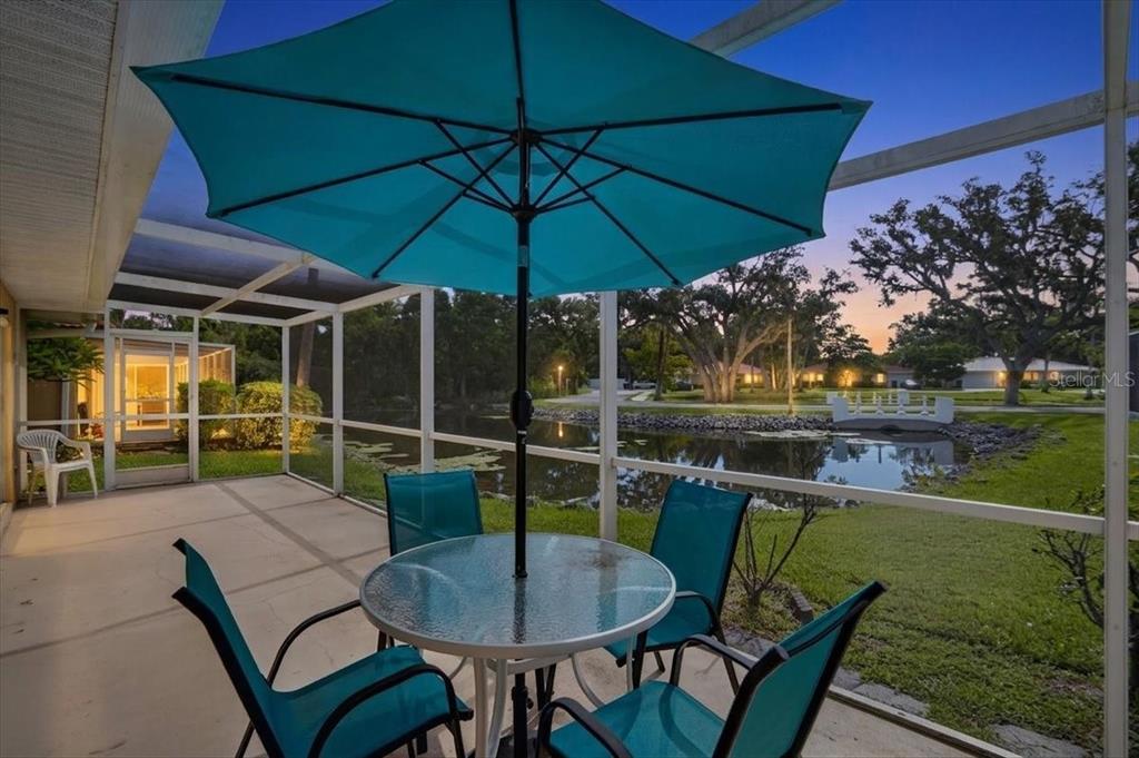 A screened-in patio features a glass-top table, teal chairs, and an umbrella overlooking a pond — 122 49TH COURT E, PALMETTO, FL
