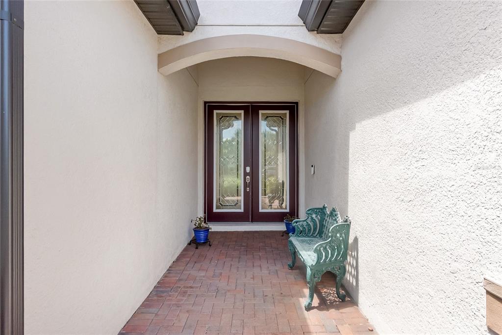 A covered entryway features a brick floor, a green metal bench, and double glass doors — 9730 CARNOUSTIE PLACE, BRADENTON, FL