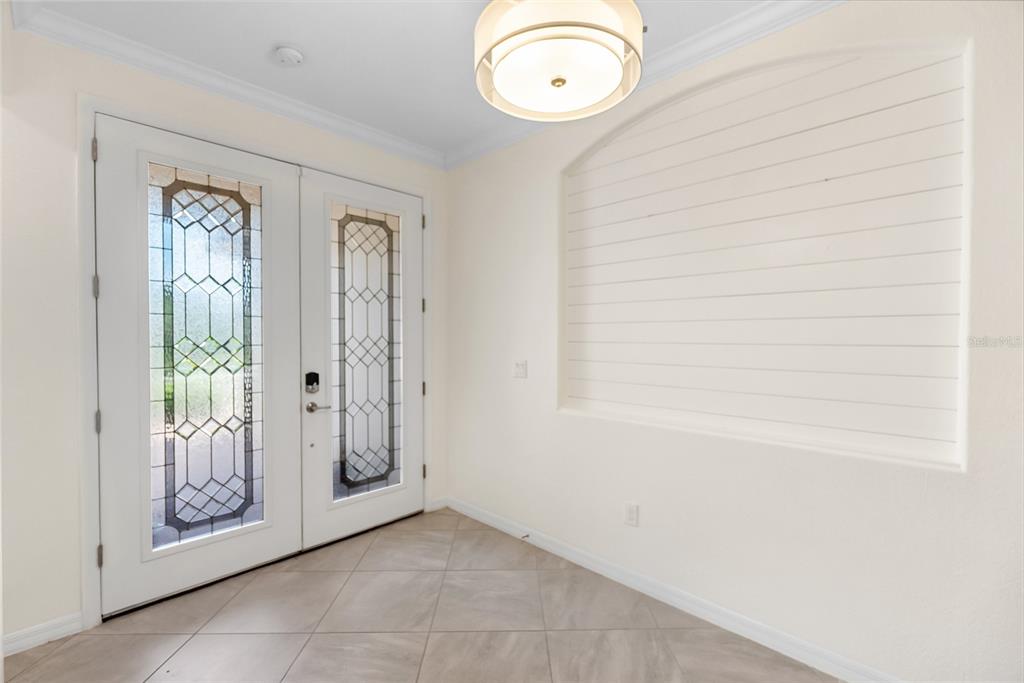 An entryway features a double front door with glass inserts, tile flooring, and shiplap wall detail — 9730 CARNOUSTIE PLACE, BRADENTON, FL