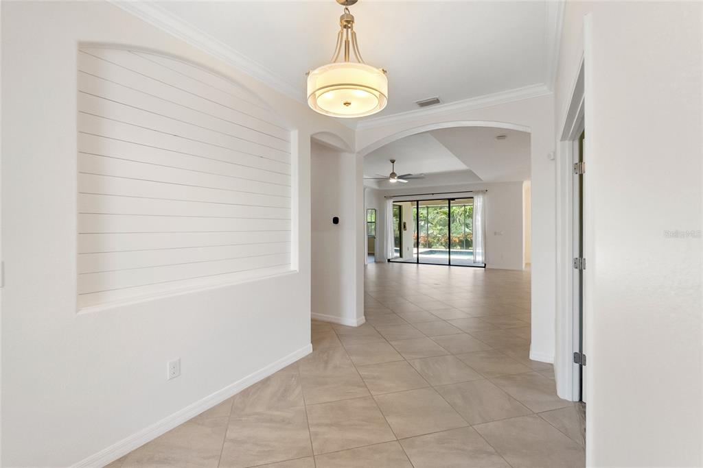 An entryway with shiplap wall detail leads into a tiled living area with pool views — 9730 CARNOUSTIE PLACE, BRADENTON, FL