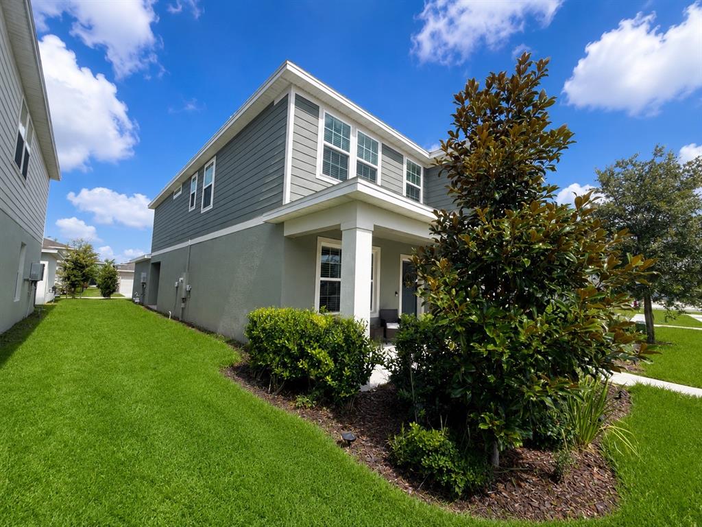 A two-story house with gray siding and stucco exterior features a side porch and lawn — 4086 LUSH VIEW DRIVE, APOPKA, FL