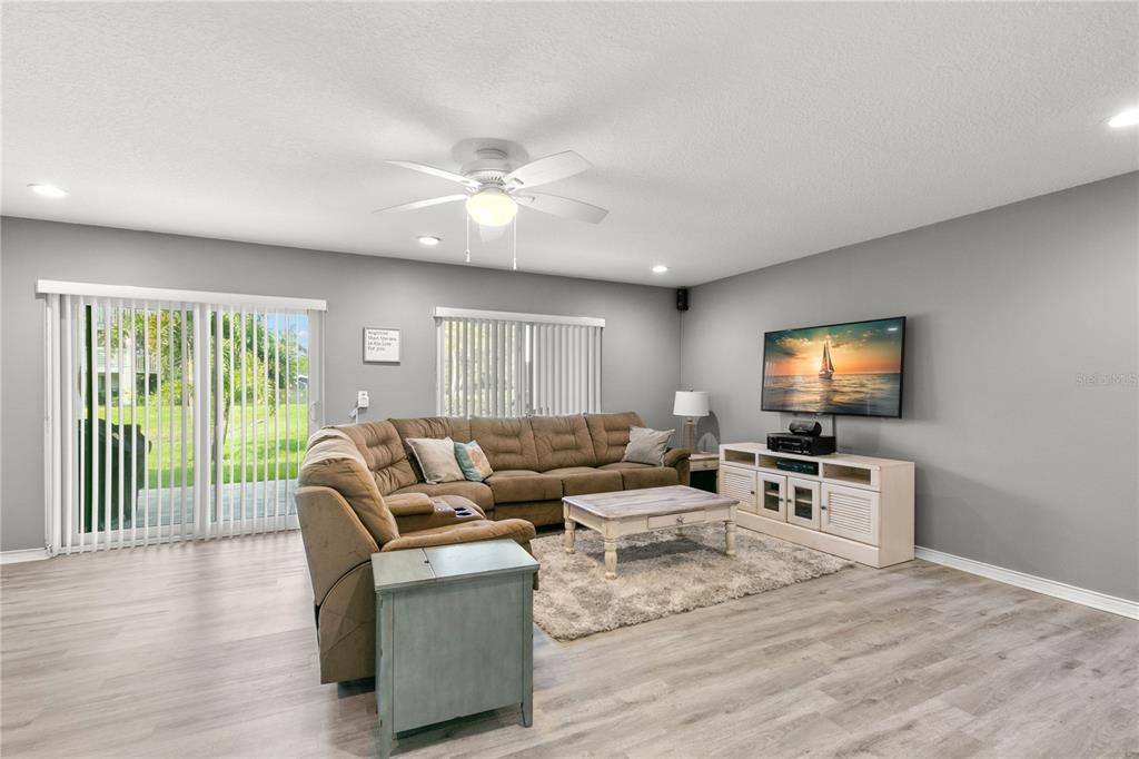 A living room features a brown sectional sofa, a television, and a sliding glass door — 2376 HANOVER DRIVE, DUNEDIN, FL