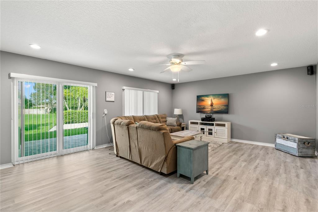 A living room with gray walls, light wood-look flooring, a sectional sofa, and sliding glass doors — 2376 HANOVER DRIVE, DUNEDIN, FL