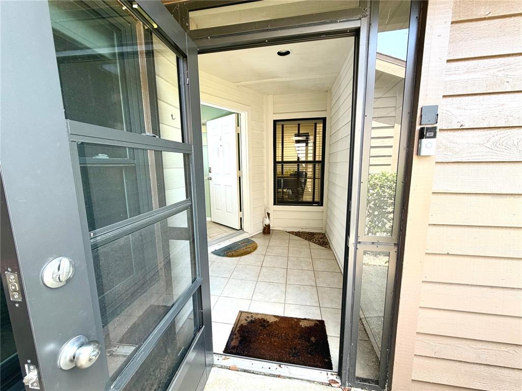 An open screen door reveals a tiled entryway leading to a white front door — 5813 MERION WAY UNIT 5813, SARASOTA, FL