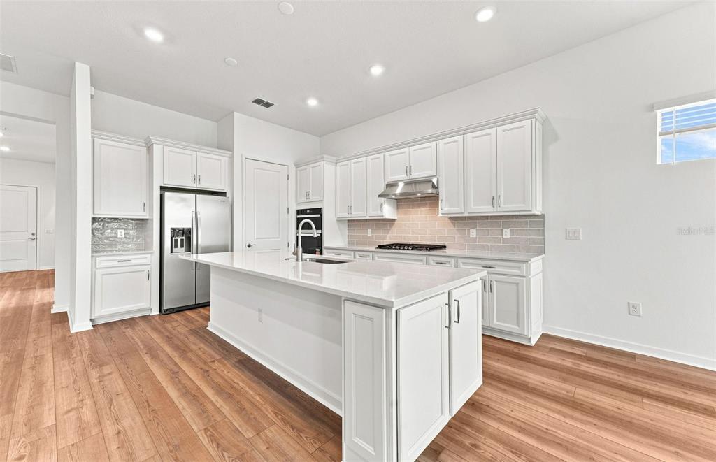 An open-concept living room and kitchen feature white cabinetry, pendant lighting, and neutral furniture — 9452 DAYLIGHT DRIVE, PARRISH, FL
