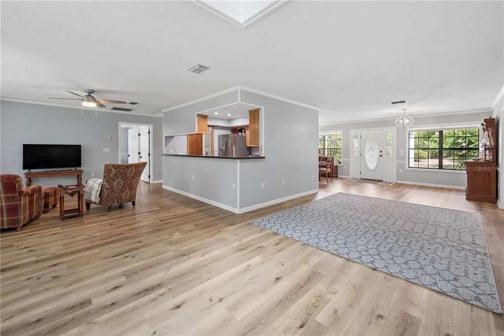 An open-concept living area features light wood flooring, gray walls, and a central kitchen pass-through — 10283 RIVER WOOD DRIVE, LIVE OAK, FL