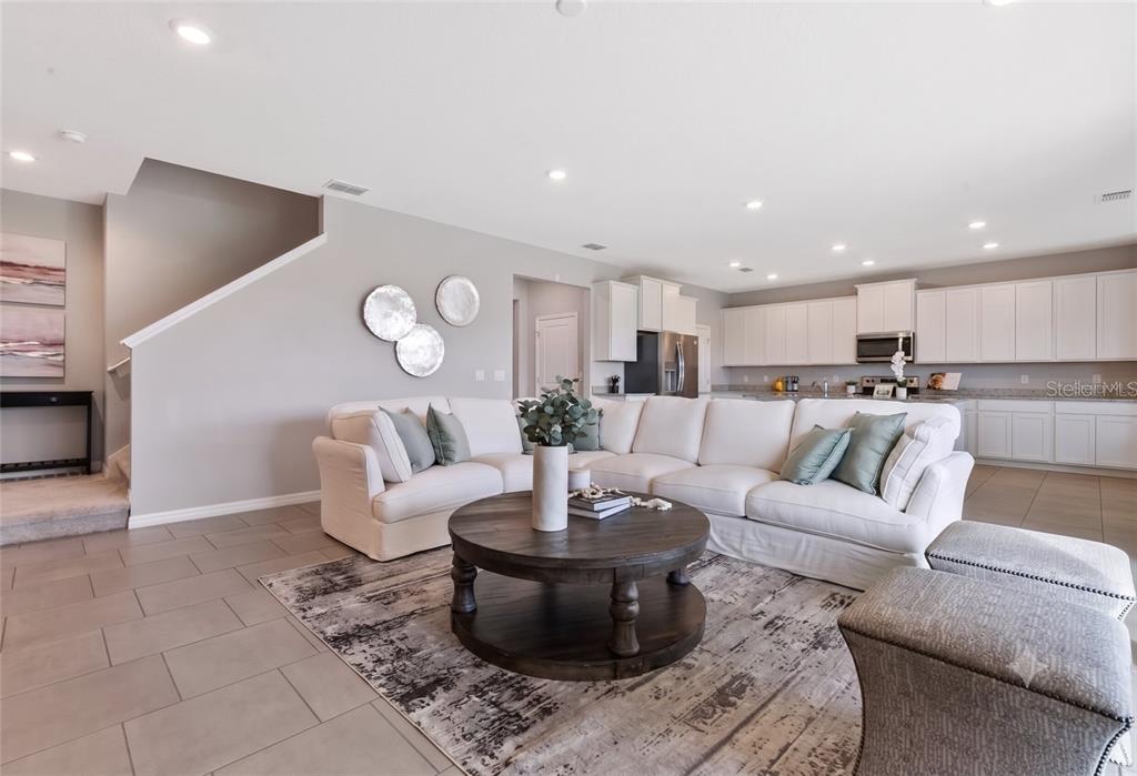 A bright open-concept living room features a white sectional sofa, round wooden coffee table, and kitchen — 13017 WILLOW GROVE DRIVE, RIVERVIEW, FL