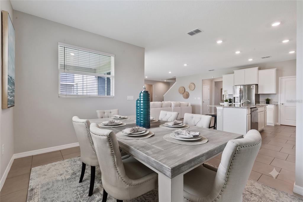 A dining room with a gray wooden table, upholstered chairs, and an open-concept kitchen — 13017 WILLOW GROVE DRIVE, RIVERVIEW, FL