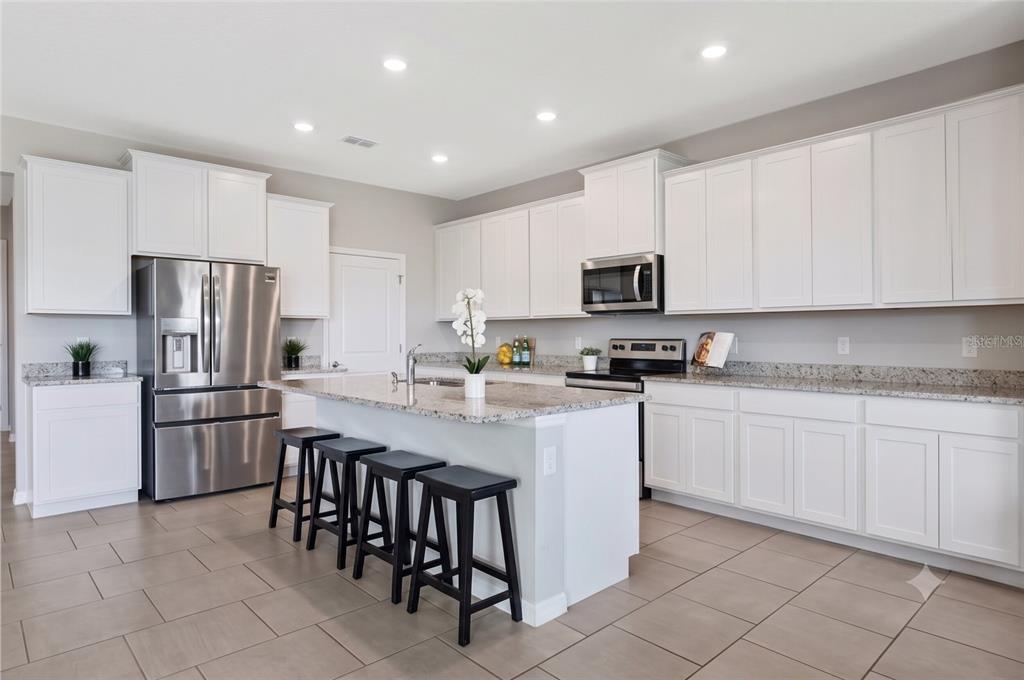 A modern kitchen features white cabinets, granite countertops, stainless steel appliances, and a breakfast island — 13017 WILLOW GROVE DRIVE, RIVERVIEW, FL