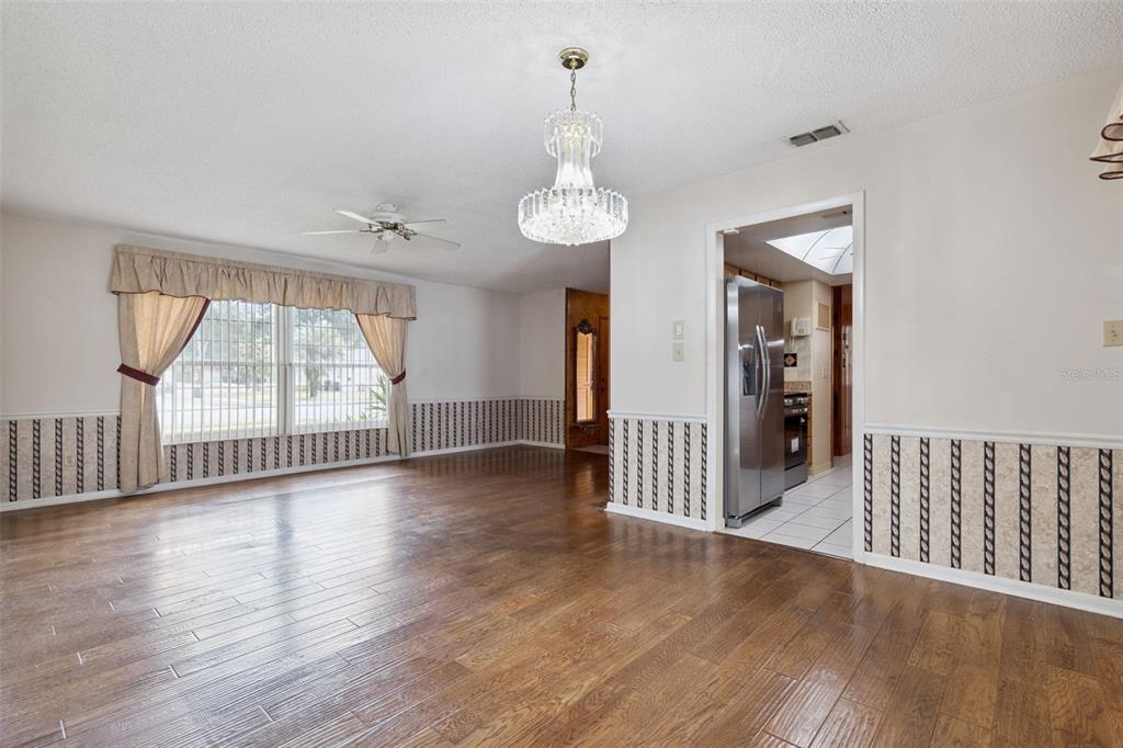 A dining room features wood-look flooring, wallpapered wainscoting, a crystal chandelier, and an adjacent kitchen — 1391 AVALON BOULEVARD, CASSELBERRY, FL