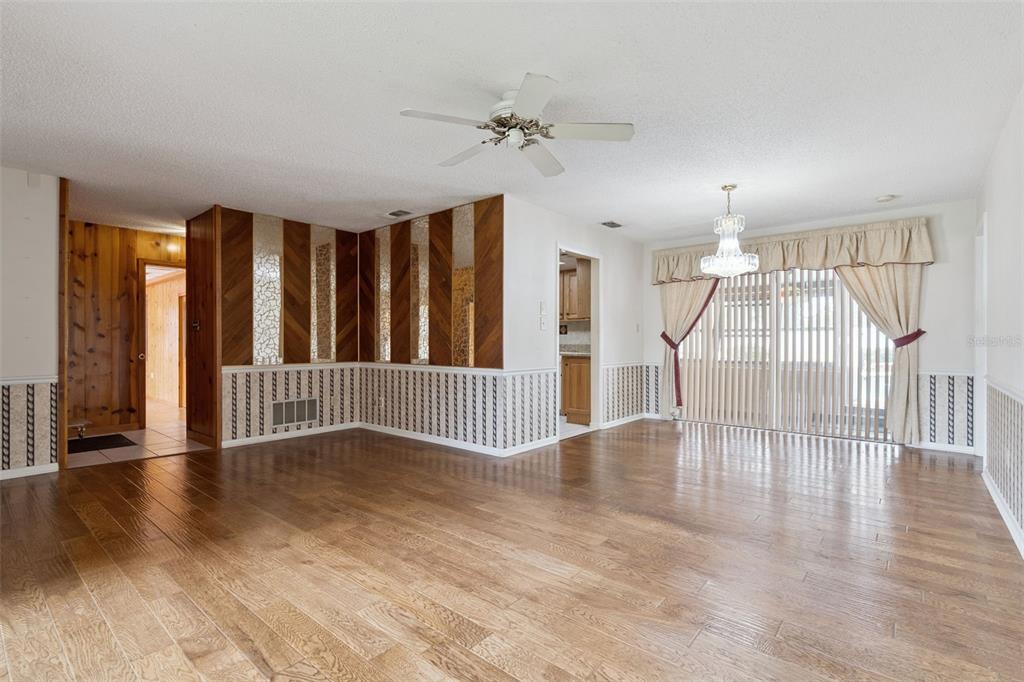 A living room features wood-look flooring, wood-paneled accent walls with mirrors, and a sliding glass door — 1391 AVALON BOULEVARD, CASSELBERRY, FL
