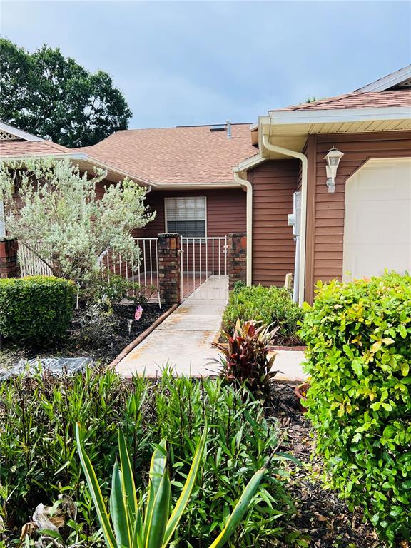 A brown-sided house features a concrete walkway leading to a gated entry and a garage — 5440 ROSEWALL CIRCLE, LEESBURG, FL