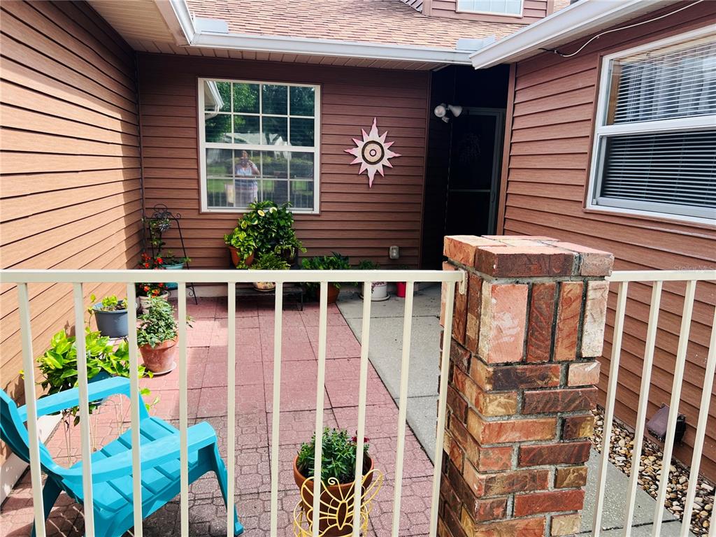 A patio with a brick pillar, metal railing, potted plants, and a blue chair — 5440 ROSEWALL CIRCLE, LEESBURG, FL