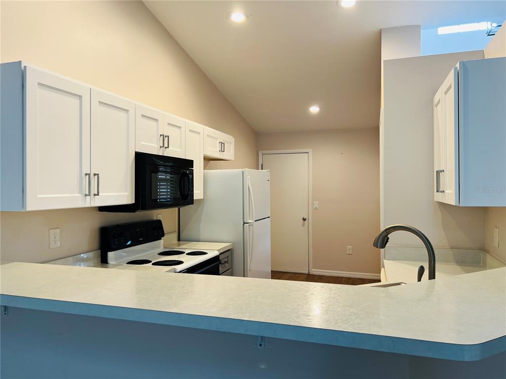 A kitchen features white cabinets, a white refrigerator, a black microwave, and a breakfast bar — 5440 ROSEWALL CIRCLE, LEESBURG, FL