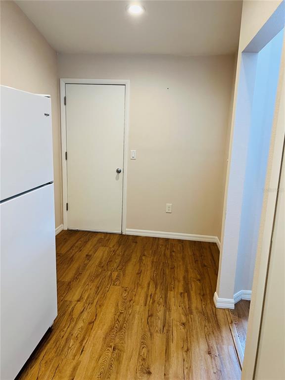 A room with wood-look flooring, a white refrigerator, and a closed door — 5440 ROSEWALL CIRCLE, LEESBURG, FL