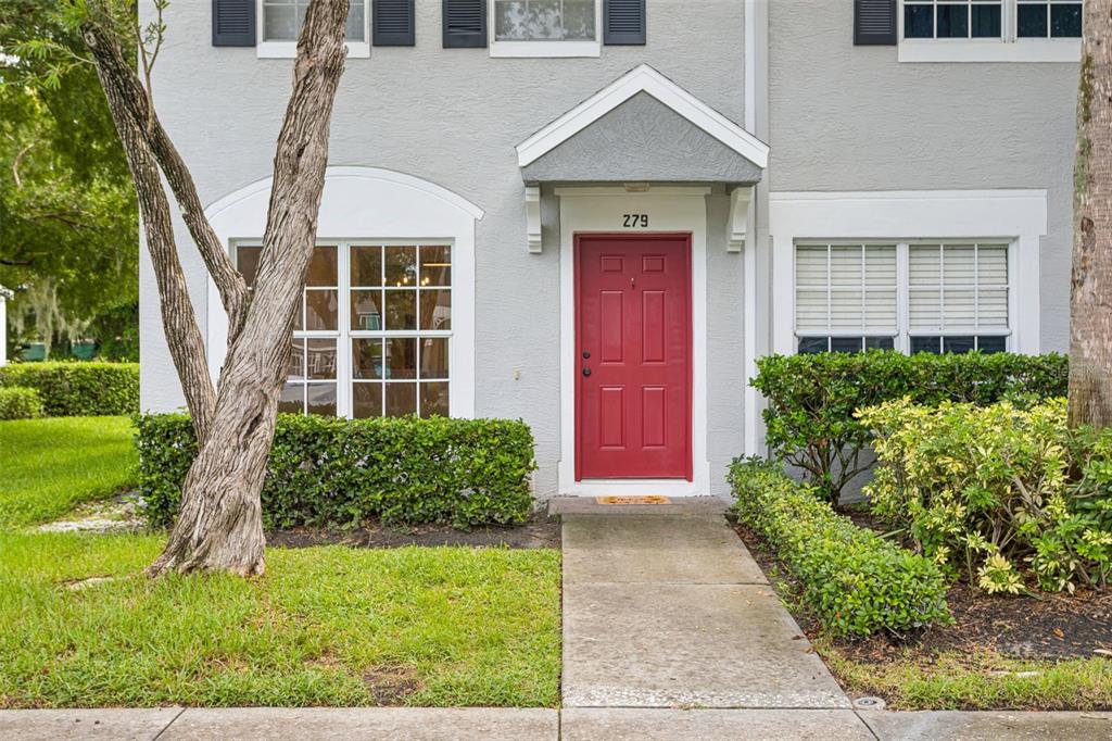 A gray two-story townhouse features a red front door, a concrete walkway, and landscaped shrubs — 279 COUNTRYSIDE KEY BOULEVARD, OLDSMAR, FL