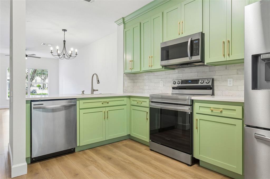 A kitchen features light green cabinets, stainless steel appliances, white countertops, and wood-look flooring — 279 COUNTRYSIDE KEY BOULEVARD, OLDSMAR, FL