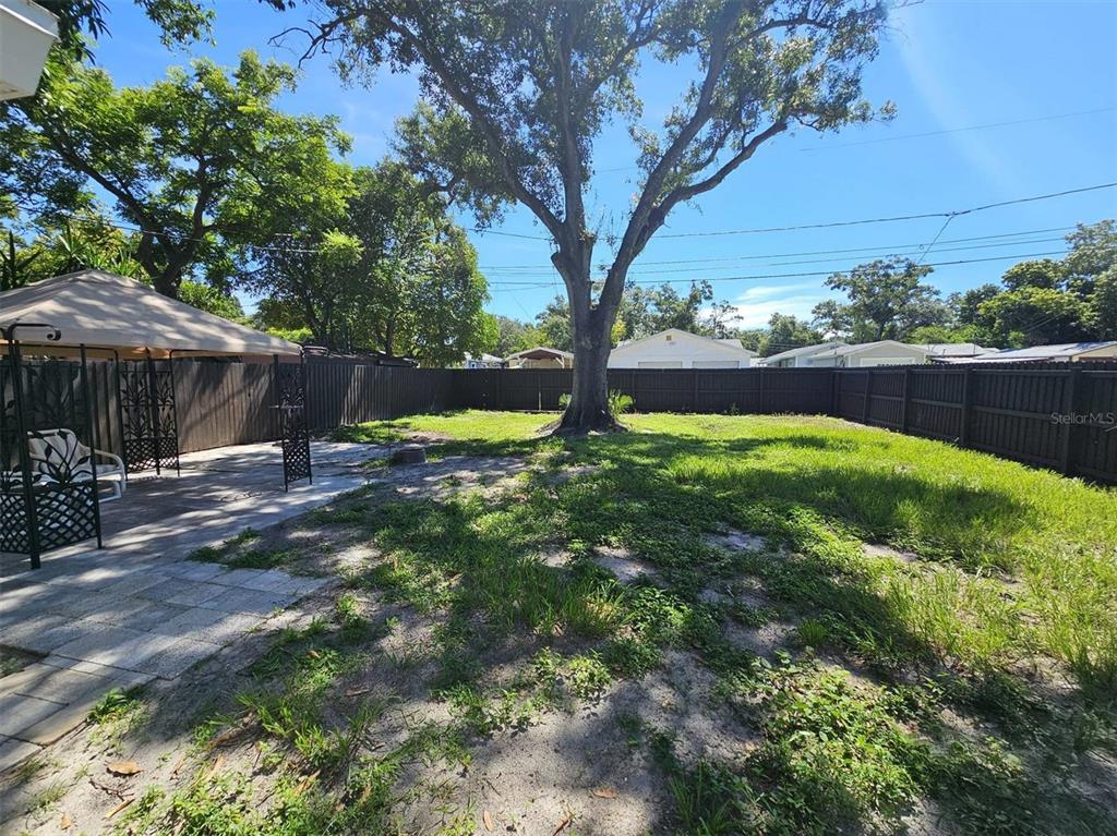A fenced backyard features a large tree, a paved patio area, and a metal gazebo — 3113 25TH STREET N, ST PETERSBURG, FL