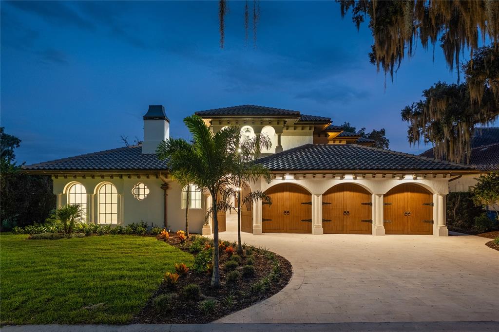 A Mediterranean-style house at dusk features a three-car garage and a curved paved driveway — 800 W 2ND AVENUE, WINDERMERE, FL