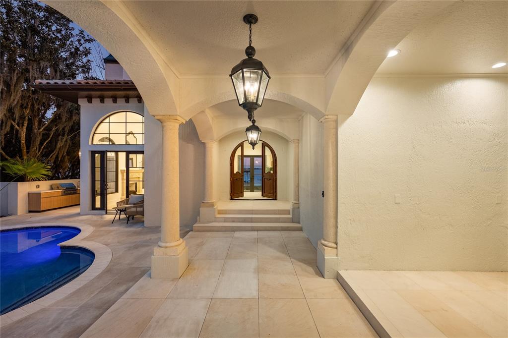A covered patio with stone flooring overlooks a swimming pool and an arched entryway — 800 W 2ND AVENUE, WINDERMERE, FL