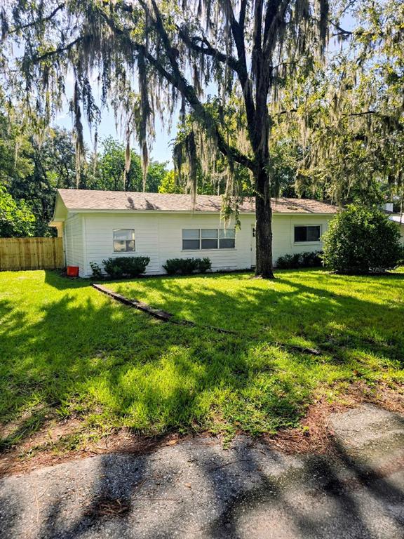 A white, single-story house with a shingled roof sits behind a large tree with moss — 3501 NW 17 TERRACE, GAINESVILLE, FL