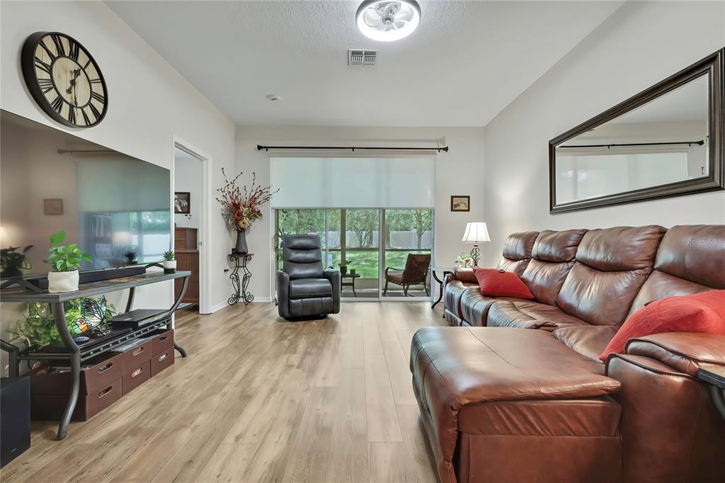 A living room features wood-look flooring, a brown leather sectional, and a large wall-mounted television — 15036 SILVERSMITH CIRCLE, SPRING HILL, FL