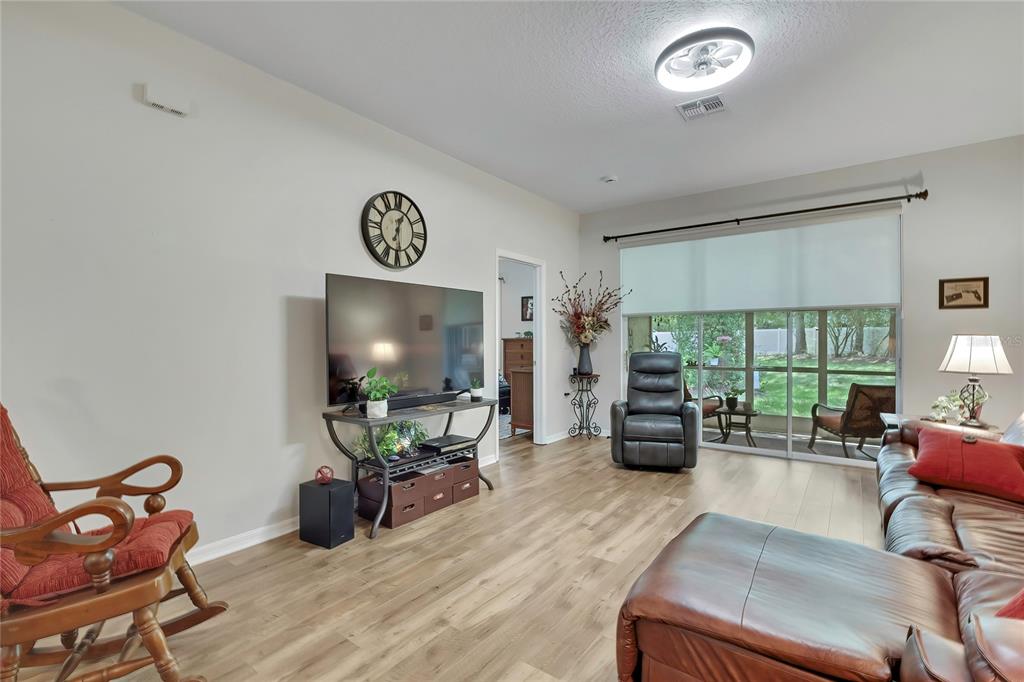 A living room features wood-look flooring, a television on a stand, and a sliding glass door — 15036 SILVERSMITH CIRCLE, SPRING HILL, FL