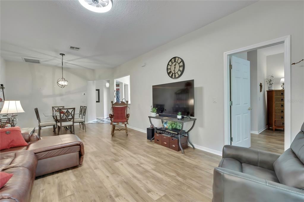 A living room with wood-look flooring, a television on a stand, and an adjacent dining area — 15036 SILVERSMITH CIRCLE, SPRING HILL, FL