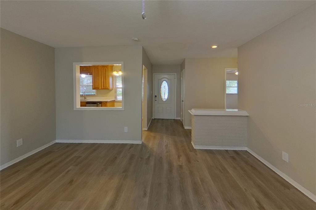 An interior view shows a living area with wood-look flooring, a pass-through window, and an entryway — 2022 68TH AVENUE S, ST PETERSBURG, FL