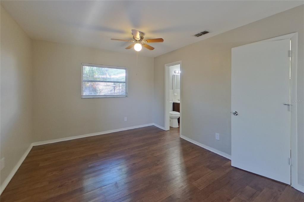 An empty bedroom features wood-look flooring, a ceiling fan, a window, and an attached bathroom — 2022 68TH AVENUE S, ST PETERSBURG, FL