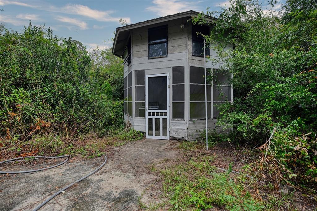A screened-in porch features stone walls, tile flooring, and a view of the wooded yard — 2424 NE 170TH STREET, CITRA, FL