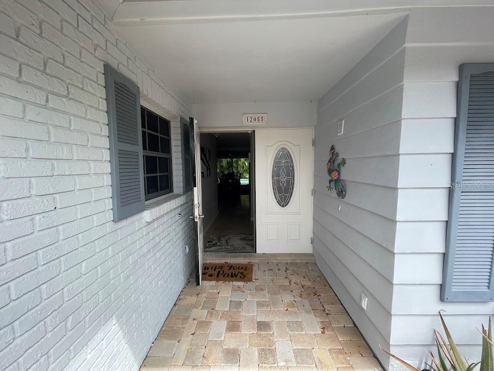 A front entryway features a paved porch, a white door with an oval window, and shutters — 12055 4TH STREET E, TREASURE ISLAND, FL