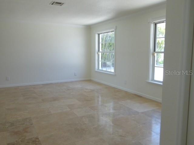 An empty room features light-colored tile flooring and two windows overlooking greenery — 12055 4TH STREET E, TREASURE ISLAND, FL