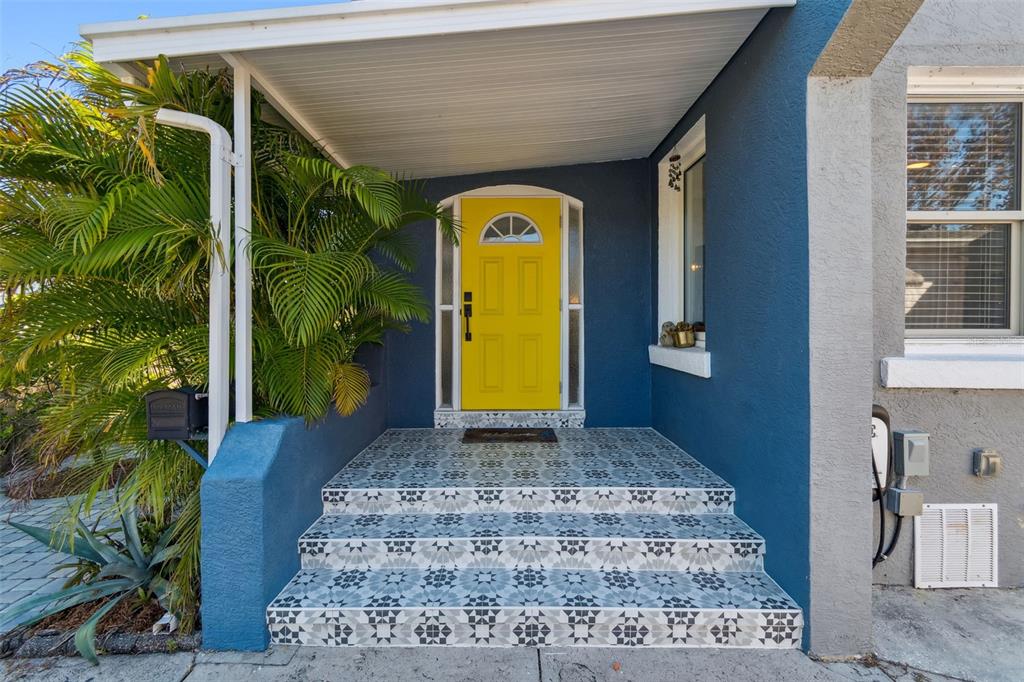 A bright yellow front door is centered above tiled steps leading to a blue house — 1120 17TH AVENUE N, ST PETERSBURG, FL