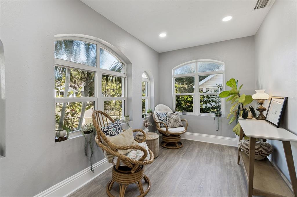 A sunroom features light gray walls, wood-look flooring, arched windows, and two rattan swivel chairs — 1120 17TH AVENUE N, ST PETERSBURG, FL