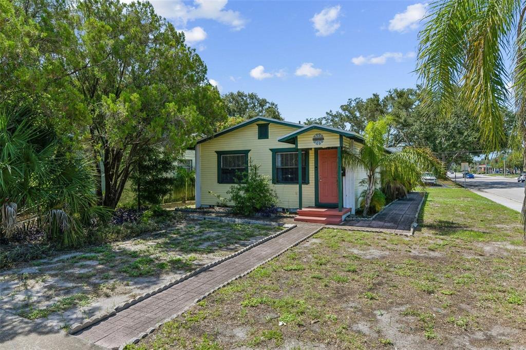 A yellow, single-story house with a red door and a brick walkway sits on grass — 5762 2ND AVENUE N, ST PETERSBURG, FL