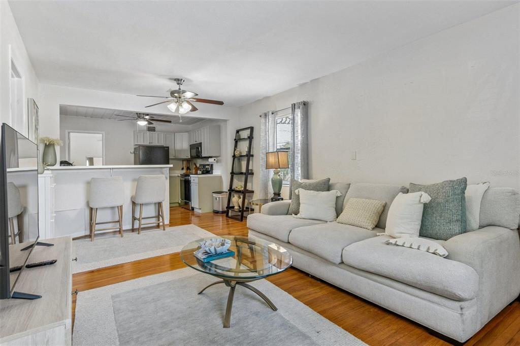 A living room with hardwood floors, a light gray sofa, and an open kitchen area — 5762 2ND AVENUE N, ST PETERSBURG, FL