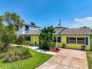 A yellow two-story house with a concrete driveway and a green lawn under a blue sky — 205 RITA BOULEVARD, MELBOURNE BEACH, FL