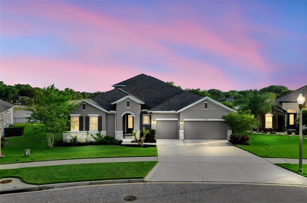 A single-story gray house with a three-car garage and a landscaped front lawn at sunset — 17060 SECRET HOLLOW LOOP, CLERMONT, FL