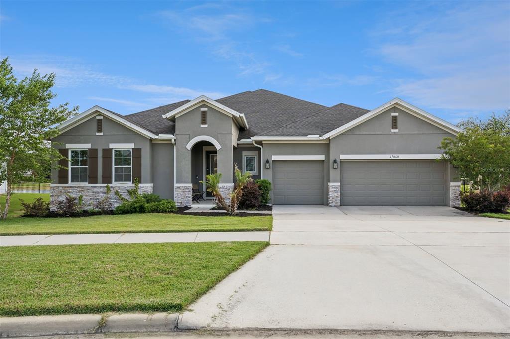 A single-story house with a gray stucco exterior, stone accents, and a three-car garage — 17060 SECRET HOLLOW LOOP, CLERMONT, FL