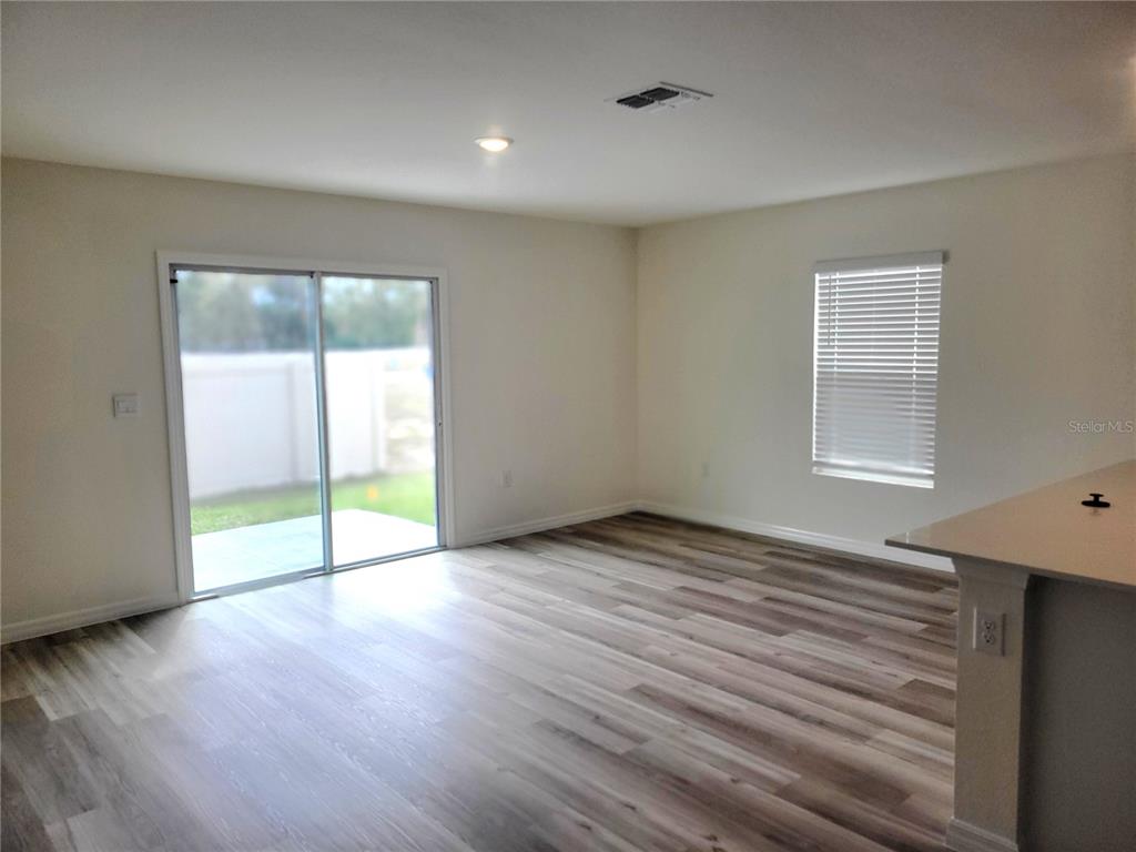An empty room features wood-look flooring, a sliding glass door, and a window with blinds — 6534 SW 82ND LOOP, OCALA, FL